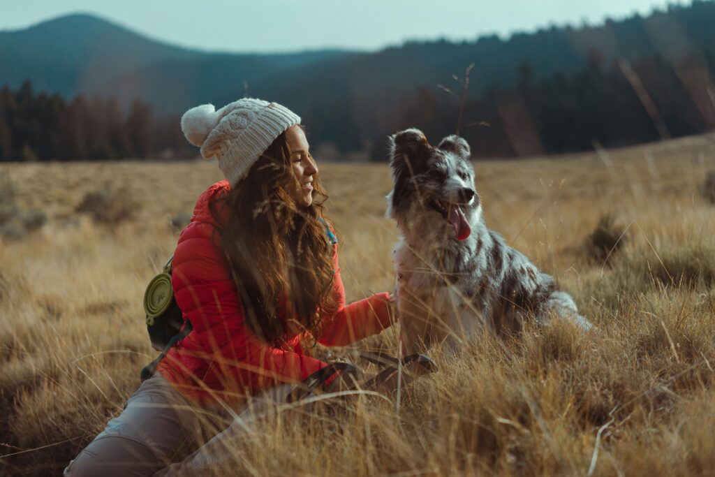 A woman travelling with her dog enjoys a serene outdoor adventure in a grassy field.