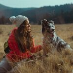 A woman travelling with her dog enjoys a serene outdoor adventure in a grassy field.